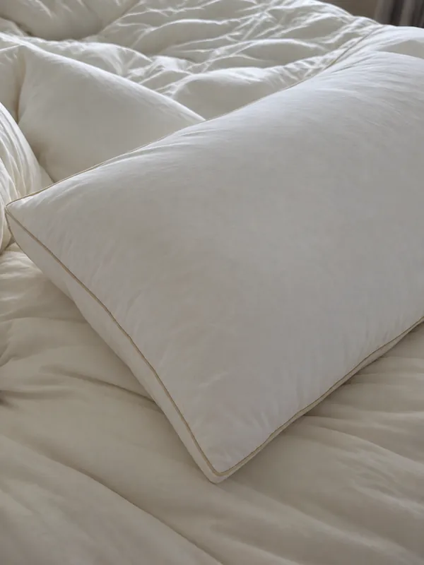 Review photo: the pillow on a bed with cream bedding, gold piping visible